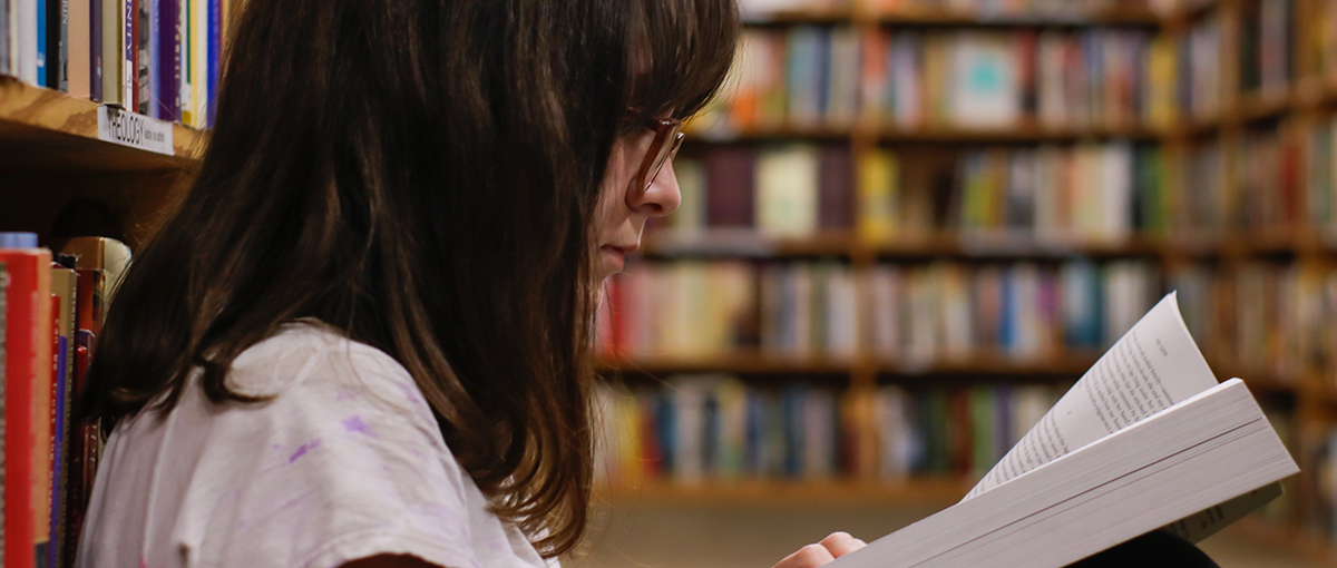 girl reading a book in library stacks