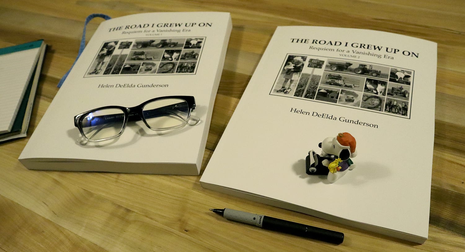 The Road I Grew Up On: Requiem for a Vanishing Era books on table with pen, glasses, and figure of Snoopy with a typewriter