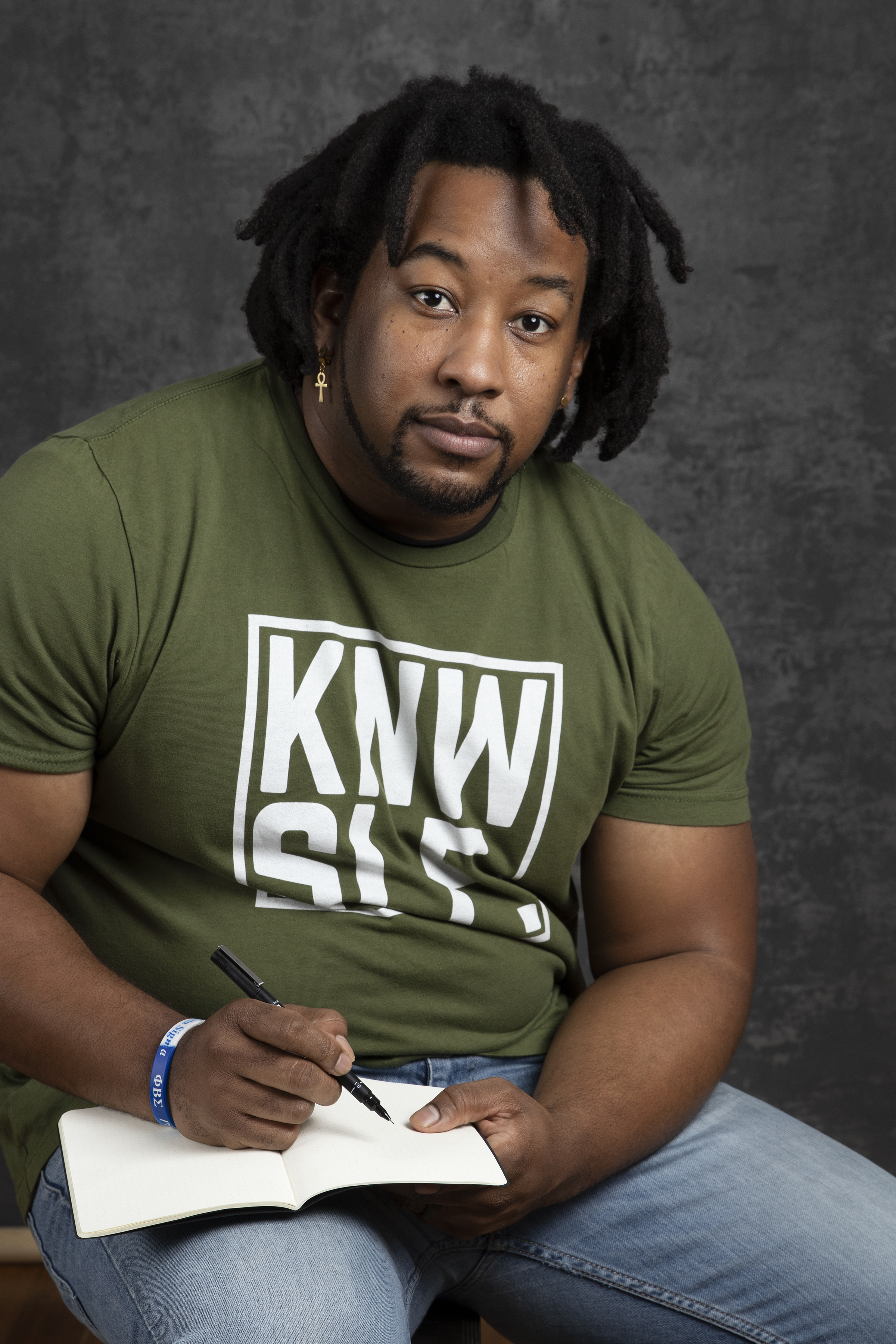 Photo of Jordan Brooks wearing a shirt with the KNWSLF logo, writing in a book