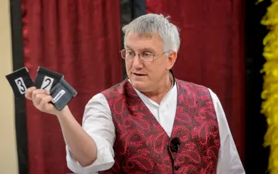 Man holding up black numbered cards in front of a red curtain