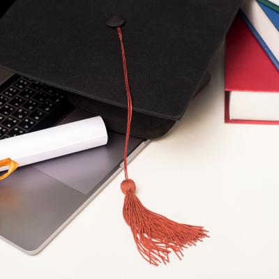 Diploma and graduation cap rest on a laptop computer with books next to it