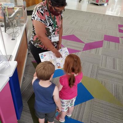 Rosie shows two children the Summer Reading Challenge game board