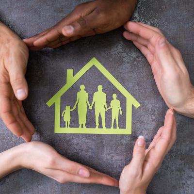 Photo of hands surrounding an cutout of a house with cutout people inside