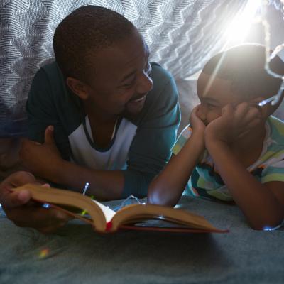 Man and child reading together in a blanket fort