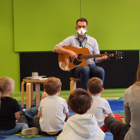 Photo of Ben playing the guitar during storytime at Ames Public Library